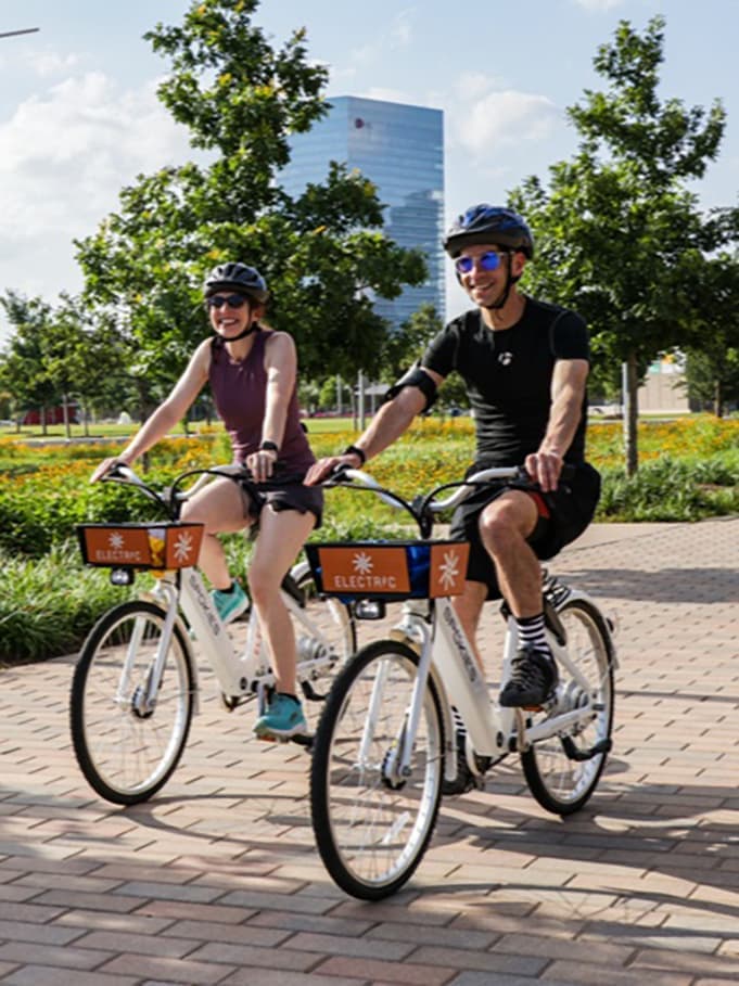 Two riders using Butterfly bike share bikes on a sunny path